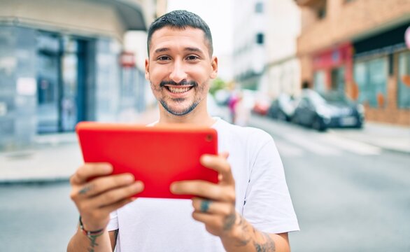 Young hispanic man using touchpad walking at street of city.
