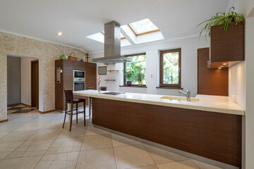 Modern spacious interior of kitchen. Wooden kitchen set with white counter. Roof window. Private house.
