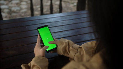 Close up of a woman's hand holding a mobile telephone with a vertical green screen in park chroma...