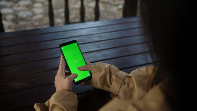 Close up of a woman's hand holding a mobile telephone with a vertical green screen in park chroma key smart phone technology cell phone, technology and lifestyle concept