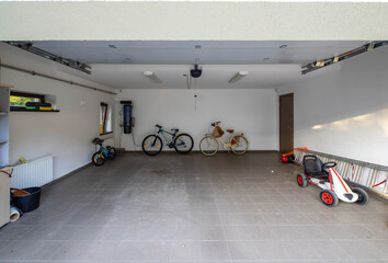 Bicycles and children's cars in the garage with tiled floor. White walls. Modern private cottage.