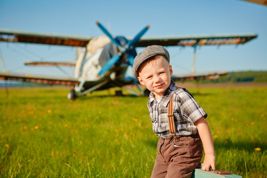 Little boy, happy kid with a small suitcase on the background of planes on the airfield. The child dreams of travelling and flying on an airplane. His future profession is pilot