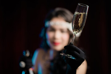 Retro styled woman dressed in Flappers dress raises glass of champagne like toast, drinking wine on velours background. Roaring twenties, retro, party, fashion concept