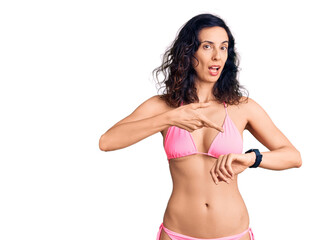 Obraz premium Young beautiful hispanic woman wearing bikini in hurry pointing to watch time, impatience, upset and angry for deadline delay