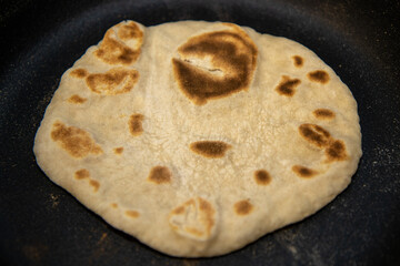 A delicious homemade flat naan bread being fried in a frying pan