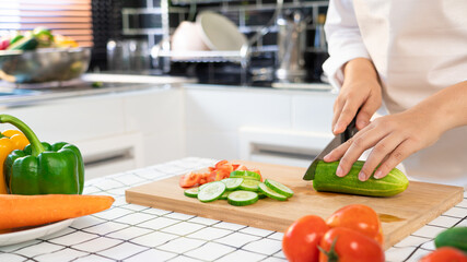 young Asian woman is preparing healthy food vegetable salad by Cutting cucumber for ingredients on cutting board on light kitchen, Cooking At Home and healthy food concept.