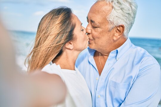 Middle age hispanic couple making selfie by the camera kissing at the beach.