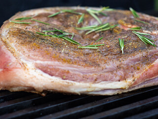 large raw steak in spices with rosemary on the grill. cooking pork leg steak with a bone.