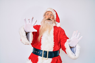 Old senior man with grey hair and long beard wearing santa claus costume with suspenders afraid and terrified with fear expression stop gesture with hands, shouting in shock. panic concept.