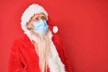 Old senior man wearing santa claus costume wearing safety mask looking to side, relax profile pose with natural face and confident smile.