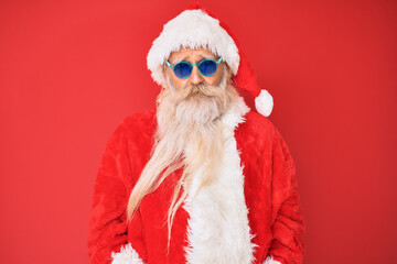 Old senior man wearing santa claus costume and sunglasses with serious expression on face. simple and natural looking at the camera.