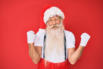Fototapeta na wymiar Old senior man with grey hair and long beard wearing white t-shirt and santa claus costume very happy and excited doing winner gesture with arms raised, smiling and screaming for success. celebration.