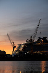 Obraz premium Silhouette of a cruise ship and tower cranes in a ship yard against sunrise