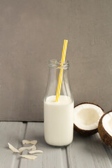 Coconut  milk in the glass bottle and coconuts on the grey  background. Location vertical.