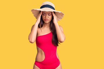Young beautiful latin girl wearing swimwear and summer hat with hand on head for pain in head because stress. suffering migraine.