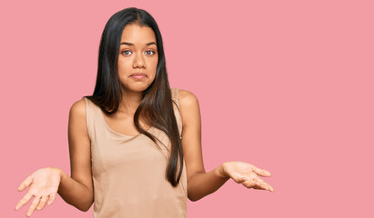 Beautiful hispanic woman wearing casual clothes clueless and confused expression with arms and...