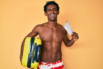 Fototapeta premium African handsome man going on summer trip holding boarding pass smiling and laughing hard out loud because funny crazy joke.