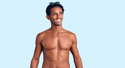 African handsome man wearing swimsuit and sunglasses looking away to side with smile on face, natural expression. laughing confident.