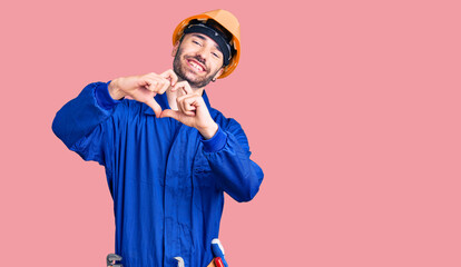 Young hispanic man wearing worker uniform smiling in love doing heart symbol shape with hands. romantic concept.