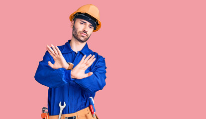 Young hispanic man wearing worker uniform rejection expression crossing arms doing negative sign, angry face