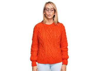 Beautiful blonde woman wearing casual clothes and glasses making fish face with lips, crazy and...