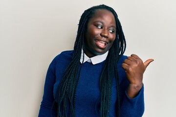 Young black woman with braids wearing casual clothes pointing thumb up to the side smiling happy with open mouth