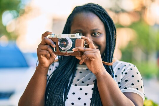 Young african american tourist woman smiling happy using vintage camera at the city.