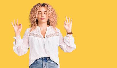 Young blonde woman with curly hair wearing elegant summer shirt relax and smiling with eyes closed doing meditation gesture with fingers. yoga concept.
