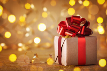 Christmas or Birthday gift box with red ribbon against golden lights and bokeh background. Holiday greeting card.