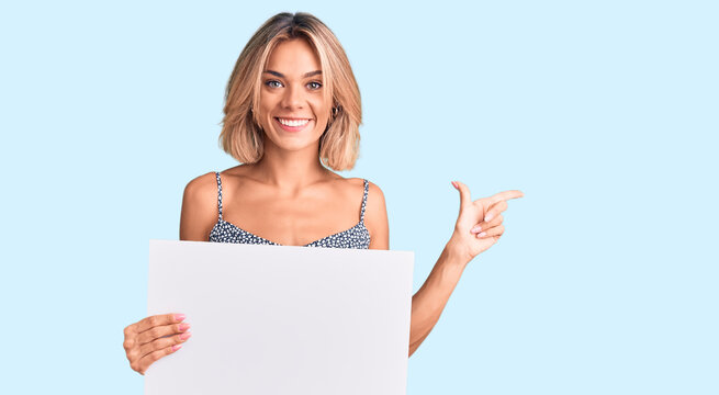 Beautiful caucasian woman holding blank empty banner smiling happy pointing with hand and finger to the side