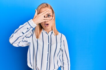 Beautiful caucasian woman wearing casual clothes and glasses peeking in shock covering face and eyes with hand, looking through fingers afraid