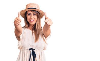 Obraz na płótnie Canvas Young beautiful woman wearing summer hat and t-shirt approving doing positive gesture with hand, thumbs up smiling and happy for success. winner gesture.