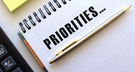 Notepad with text PRIORITIES, next to it lies a calculator and yellow note papers.