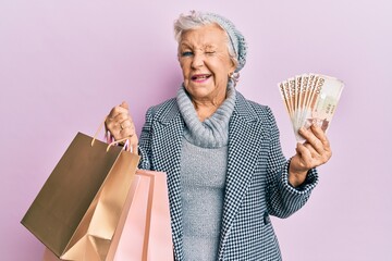 Senior grey-haired woman holding shopping bags and south korea won banknotes winking looking at the...