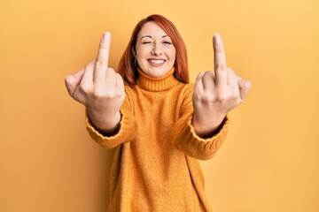 Beautiful redhead woman showing middle finger doing bad gesture winking looking at the camera with...