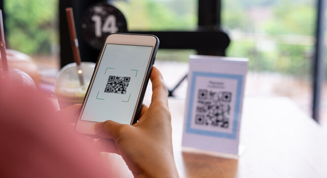 Women's hand uses a mobile phone application to scan QR codes in stores that accept digital payments without money and plastic tags on the table. QR code payment and cash technology concept