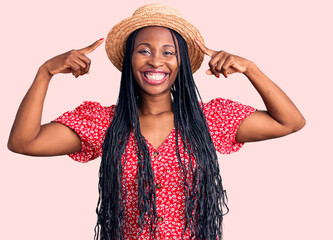 Young african american woman wearing summer hat smiling pointing to head with both hands finger, great idea or thought, good memory