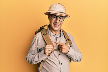 Middle age bald man wearing explorer hat and backpack smiling happy pointing with hand and finger