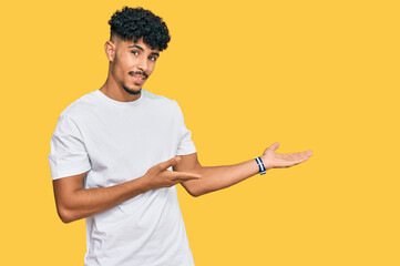 Young arab man wearing casual white t shirt inviting to enter smiling natural with open hand