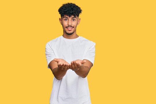 Young arab man wearing casual white t shirt smiling with hands palms together receiving or giving gesture. hold and protection