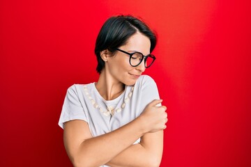 Young brunette woman with short hair wearing casual clothes and glasses hugging oneself happy and positive, smiling confident. self love and self care