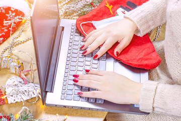 Woman hands typing on the laptop keyboard on Christmas and New Year decorations and face mask background. Online holiday shopping, study, distant communication and Xmas congratulation concept.