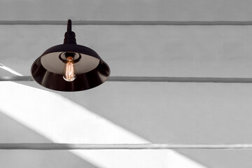iron black loft style light with an edison lamp with threads shining warm light on a white wall...