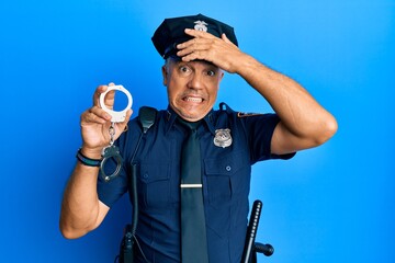 Handsome middle age mature man wearing police uniform holding metal handcuffs stressed and...