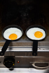 Vertical shot of two small pans on the stove and hot fried eggs being cooked on them