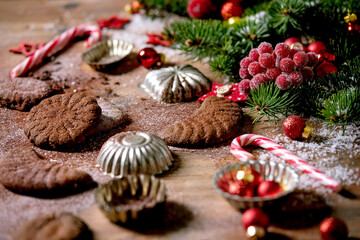 Fototapeta na wymiar Homemade traditional Christmas shortcrust cookies chocolate crescents with cocoa icing sugar in ceramic plate with cookie molds, fir tree, red xmas stars decorations over wooden background.