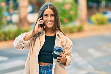 Fototapeta premium Young hispanic girl smiling happy talking on the smartphone and drinking take away coffee at the park.