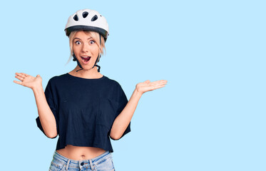 Young beautiful blonde woman wearing bike helmet celebrating victory with happy smile and winner expression with raised hands