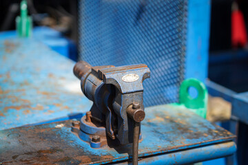 A metal beach vise in rusty condition, installed on workbench at factory's workshop. Close-up and selective focus at the vise clamping part, Industial object photo.