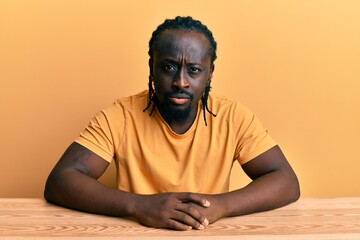 Handsome young black man wearing casual clothes sitting on the table skeptic and nervous, frowning...